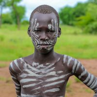 A Mursi Boy Painted in Stripes Ready to go Herd, Ethiopia